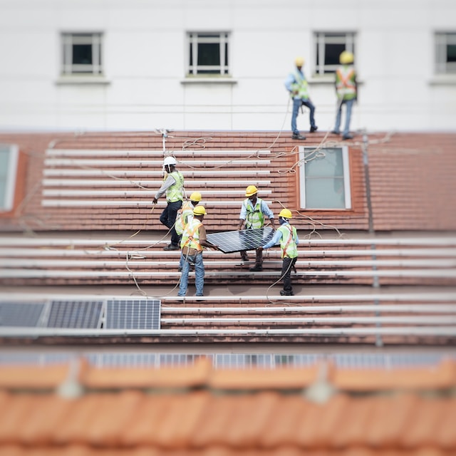 Workers carrying a piece of solar panel on top of a roof