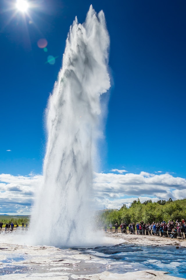 A crowd of onlookers watch a geyser spring out of the ground