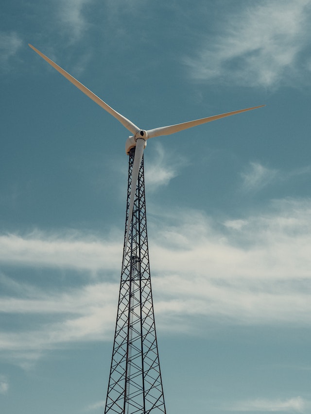 A long wind turbine against a blue sky specked with white cottony clouds